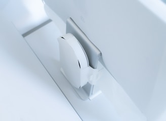 A white, sleek, vertical gaming console placed beside a large, slim monitor. The setting exudes minimalism with a focus on modern technology design.