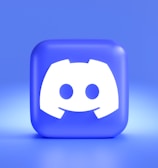 A three-dimensional blue cube featuring a white, stylized gaming controller symbol associated with a popular communication platform, set against a gradient blue background.